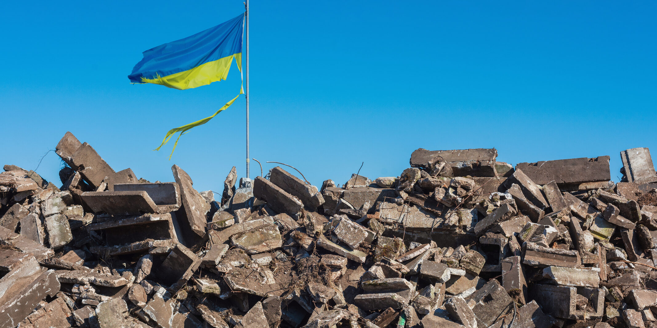 war in ukraine. Destroyed Ukrainian building and damaged flag in the wind.