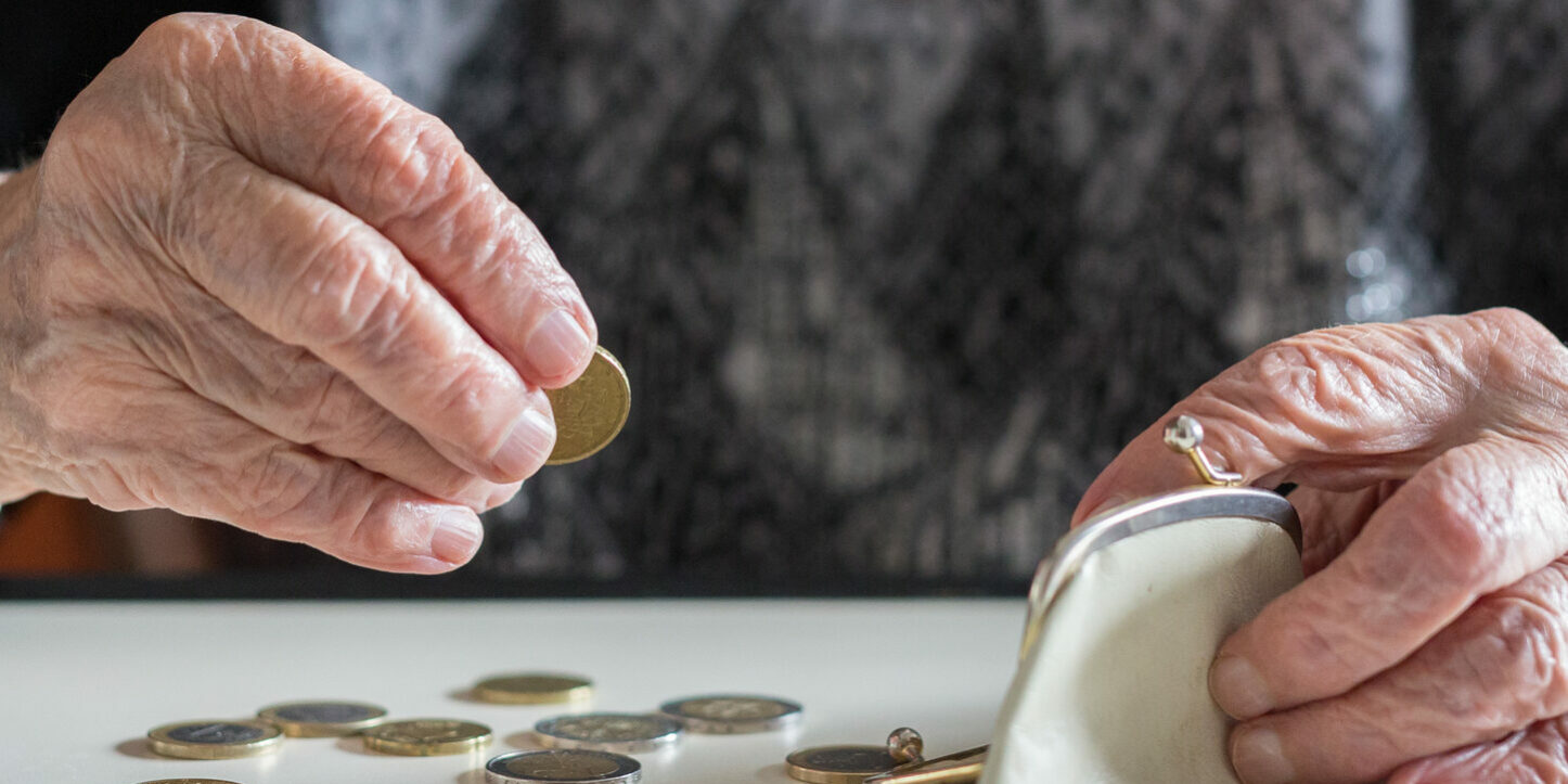 Elderly woman sitting at the table counting money in her wallet.