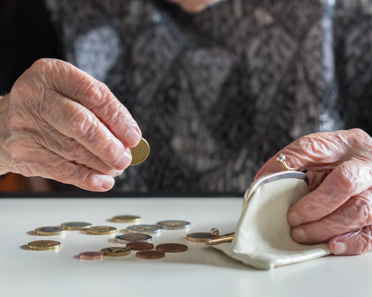 Elderly woman sitting at the table counting money in her wallet.